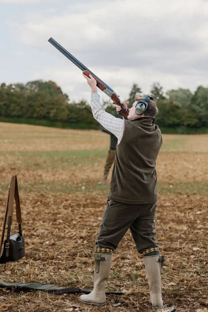 Person in forest knightwood fleece gilet aiming shotgun outdoors for hunting or shooting