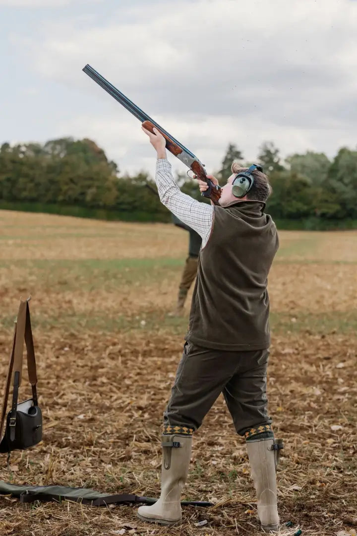 Person in forest knightwood fleece gilet aiming shotgun outdoors for hunting or shooting