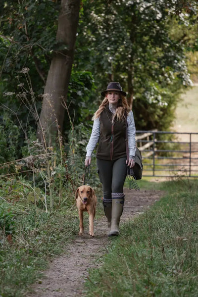 Woman in a hat and vest walking her dog in country clothing outdoors with New Forest Gilet