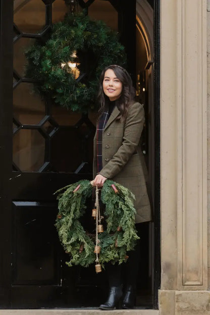 Woman holding a Christmas wreath in a stylish Forest Lizzie Tweed coat