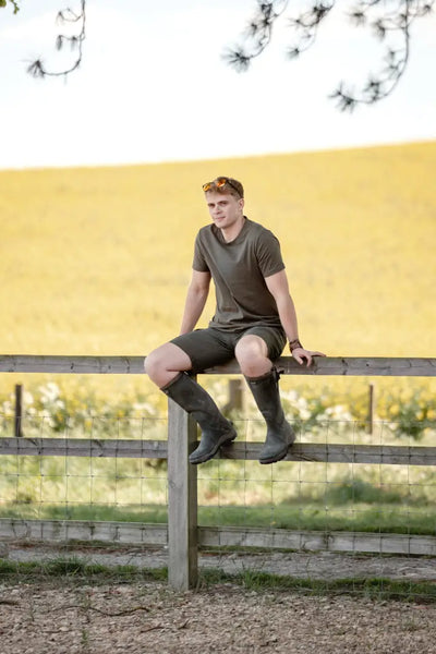 Man in olive green forest clothing graphic T-shirt sitting on wooden fence