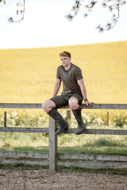 Man in olive green forest clothing graphic T-shirt sitting on wooden fence