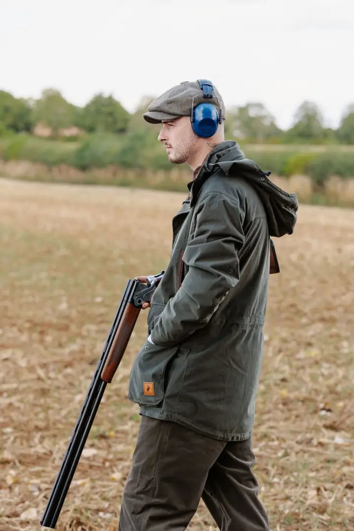 Man in hunting attire holding a shotgun wearing a New Forest Marsh Jacket in the forest
