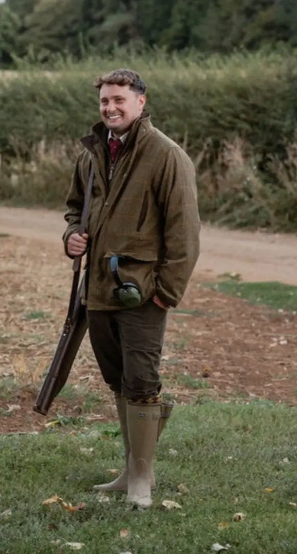 Smiling man in hunting attire with shotgun wearing New Forest Maverick waterproof tweed jacket