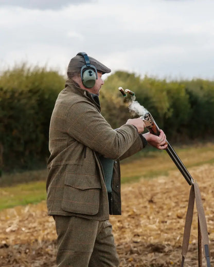 Man in tweed jacket with shotgun and smoke, showcasing the New Forest Maverick waterproof tweed jacket