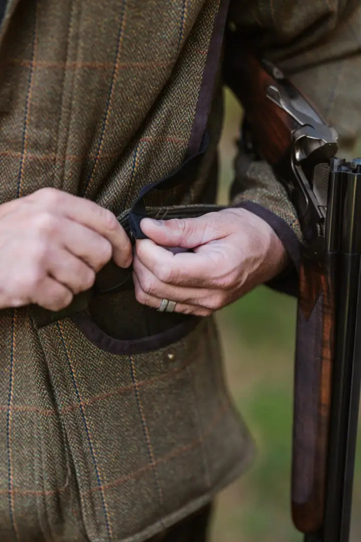 Person adjusting gun in New Forest Maverick waterproof tweed jacket, a sophisticated field coat