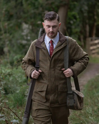 Man wearing New Forest Maverick waterproof tweed jacket with rifle and bag outdoors