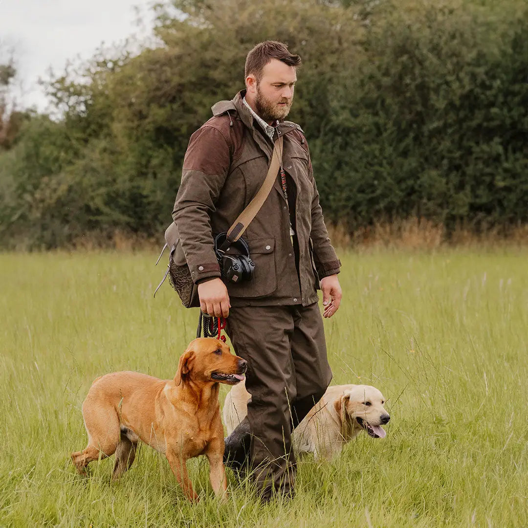 Man in New Forest Performance Field Coat walking two dogs in grassy field