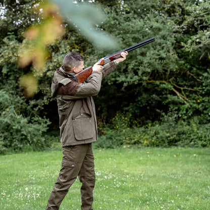 Person in hunting attire aiming shotgun while wearing New Forest Performance Field Coat