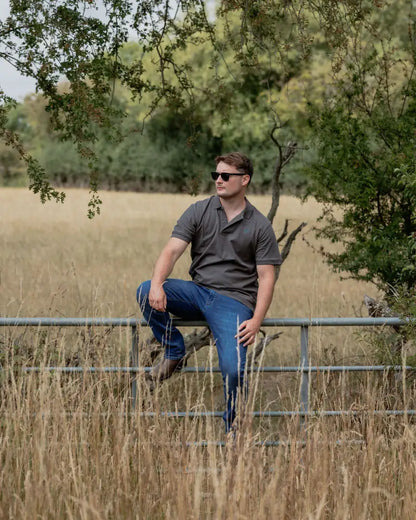 Man in sunglasses sitting on a fence wearing a New Forest Pique Polo Shirt in forest pique style