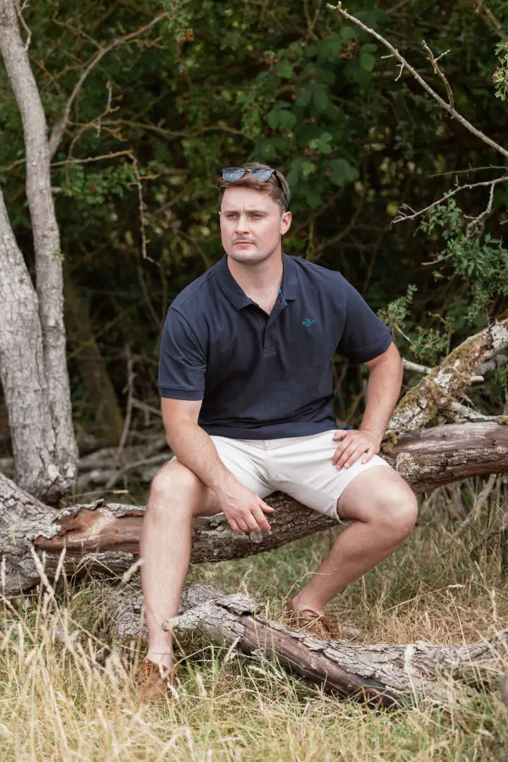 Man in forest pique polo shirt and shorts sitting on a log outdoors