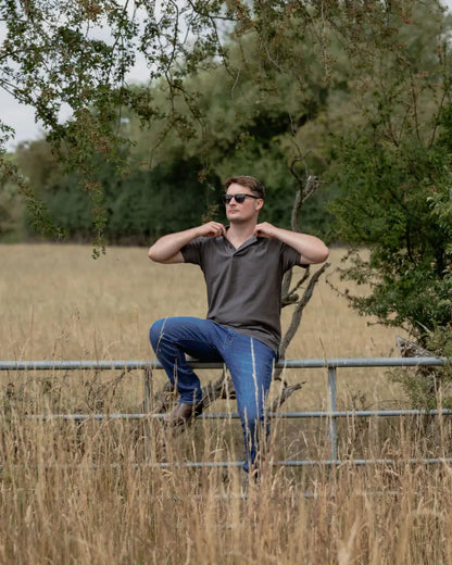 Man in sunglasses sitting on a fence wearing a New Forest Pique Polo Shirt