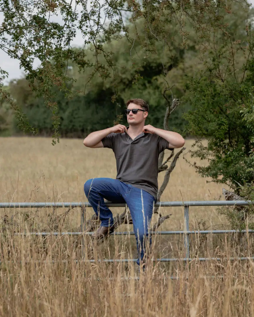 Man in sunglasses sitting on a fence wearing a New Forest Pique Polo Shirt