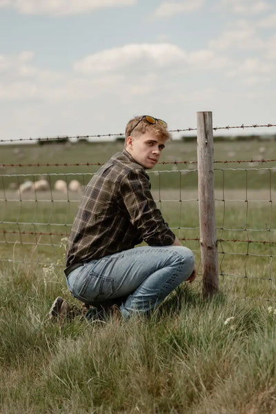 Man crouching by barbed wire wearing New Forest Premium Tattersall Shirt casual shirt boasts single chest pocket top-grade cotton