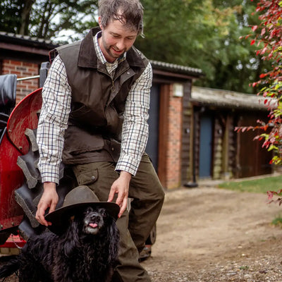 Man placing a hat on a black dog while wearing a New Forest Premium Tattersall Shirt