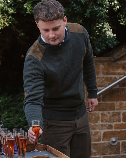Person in forest raven crew jumper with dark green sweater and brown patches holding a glass