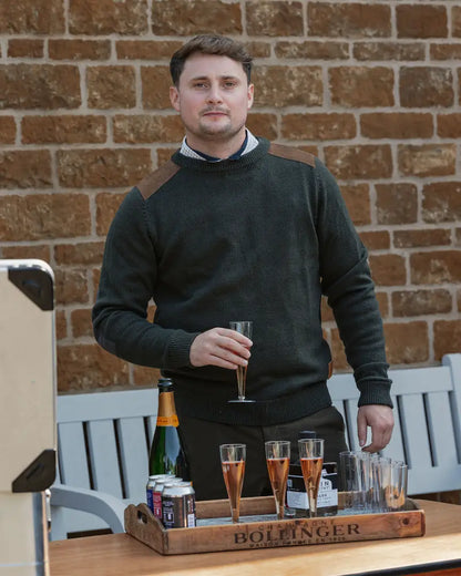 Man in dark green forest raven crew neck jumper holding champagne flute