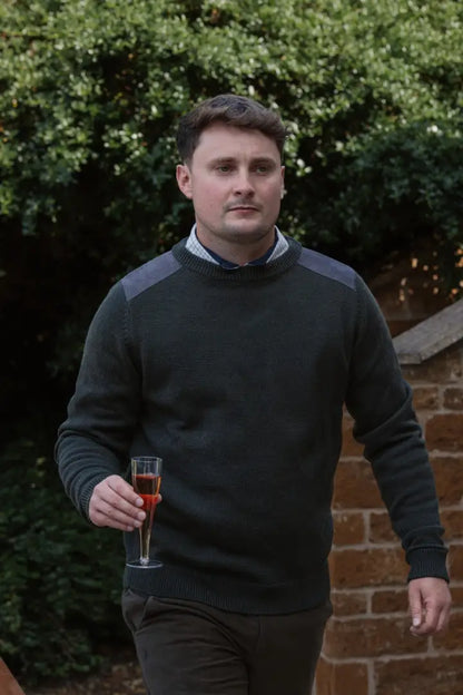 Man holding red wine wearing New Forest Raven Crew Neck Jumper in a cozy setting