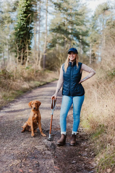 Woman walking dog on a wooded path wearing a stylish Forest Skeet Cap