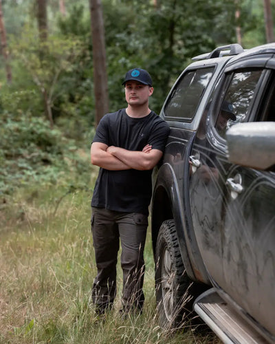 Man leaning on a dirty pickup truck wearing New Forest Trail Trousers for forest trail adventures