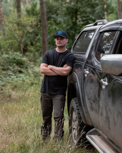 Man leaning on a dirty pickup truck wearing New Forest Trail Trousers for forest trail adventures