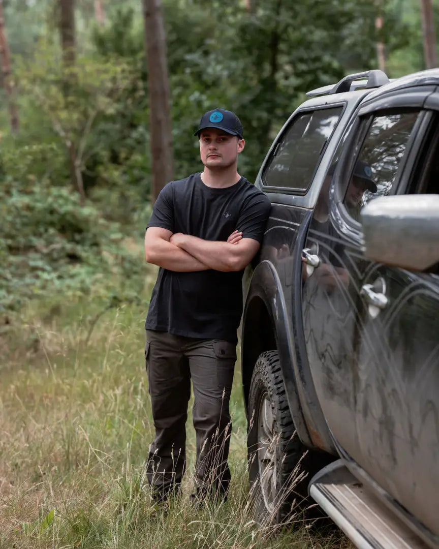 Man leaning on a dirty pickup truck wearing New Forest Trail Trousers for forest trail adventures