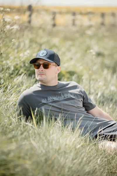Man in sunglasses and baseball cap lying in grass wearing New Forest Trucker Hat for rugged charm