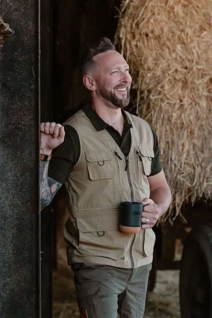 Smiling man in tan explorer gilet holding mug, perfect for forest explorer adventures