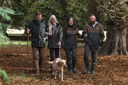 Four people and a dog in outdoor forest woodsman wax jacket walk happily