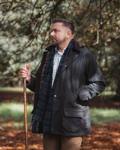 Man in forest woodsman wax jacket with plaid scarf holding walking stick outdoors