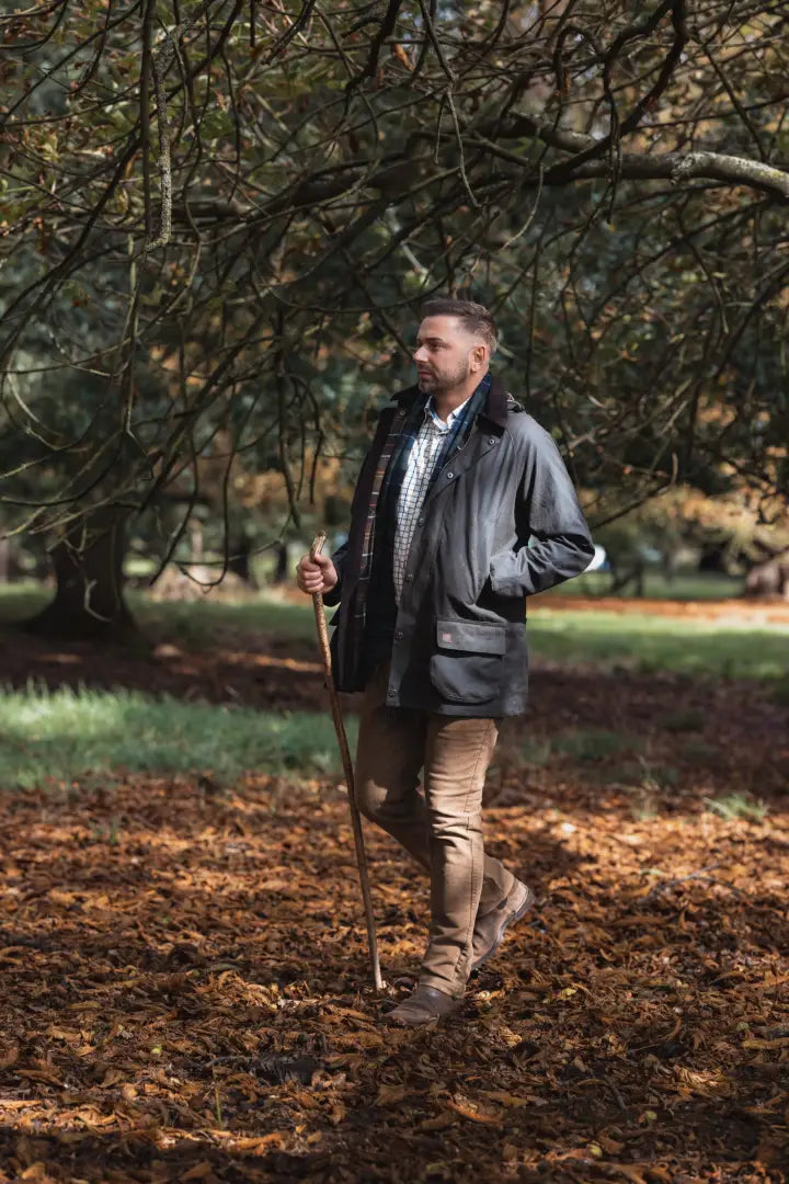 Man in dark jacket and tan pants holding walking stick in Forest Woodsman Wax Jacket