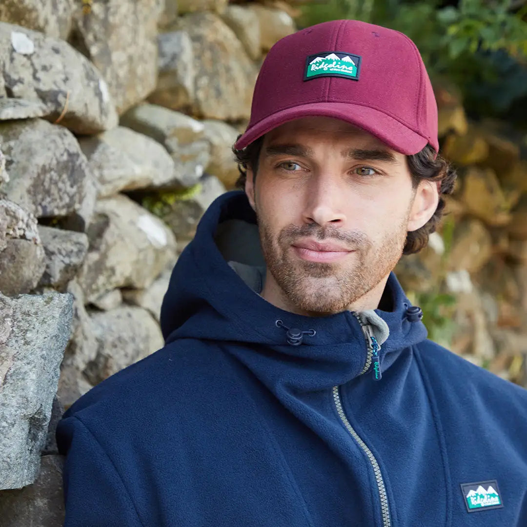 Man wearing a Ridgeline Monsoon Classic Cap with green mountain patch and navy fleece