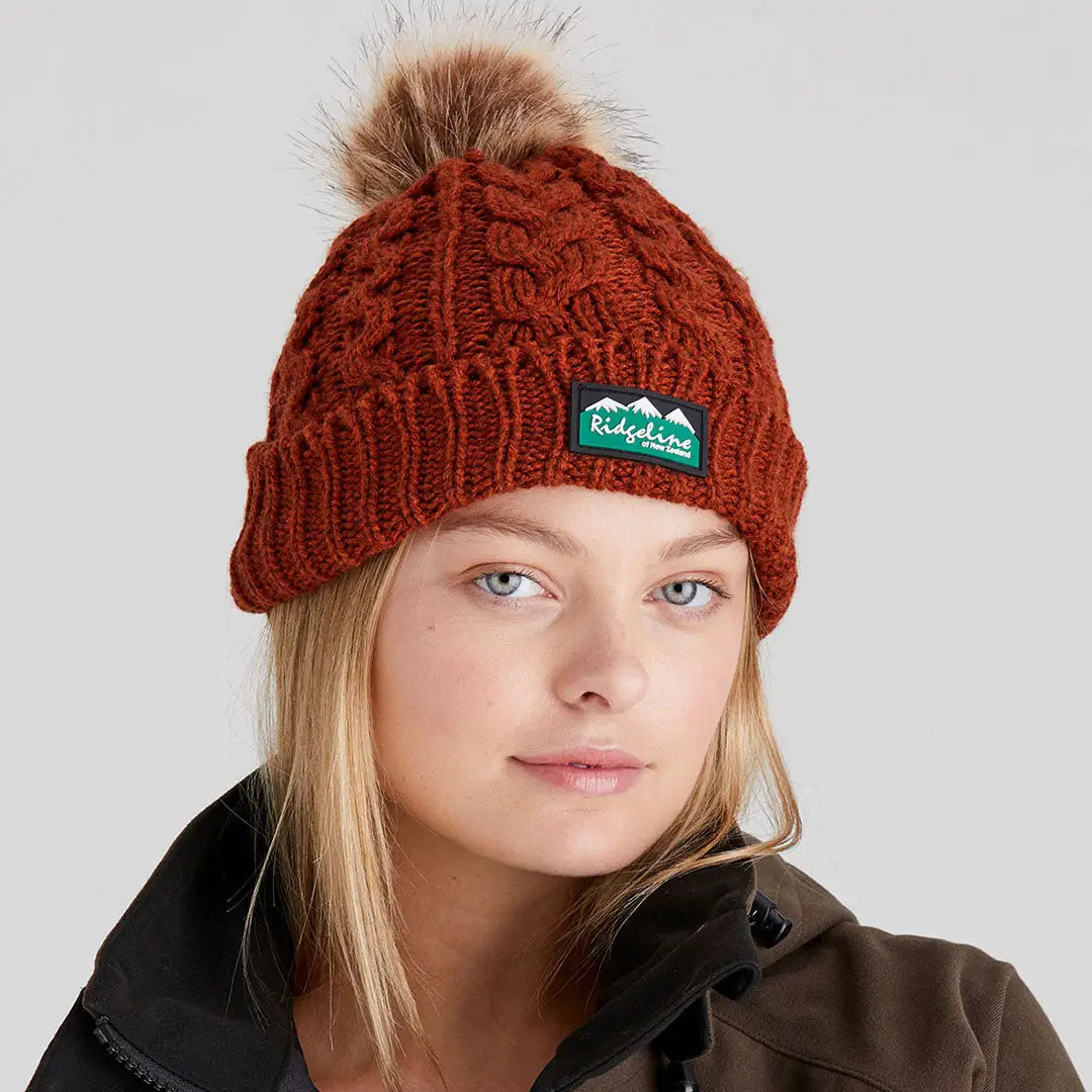 Rust-colored Nordic Fleck Bobble Hat with pom-pom and mountain patch for winter style