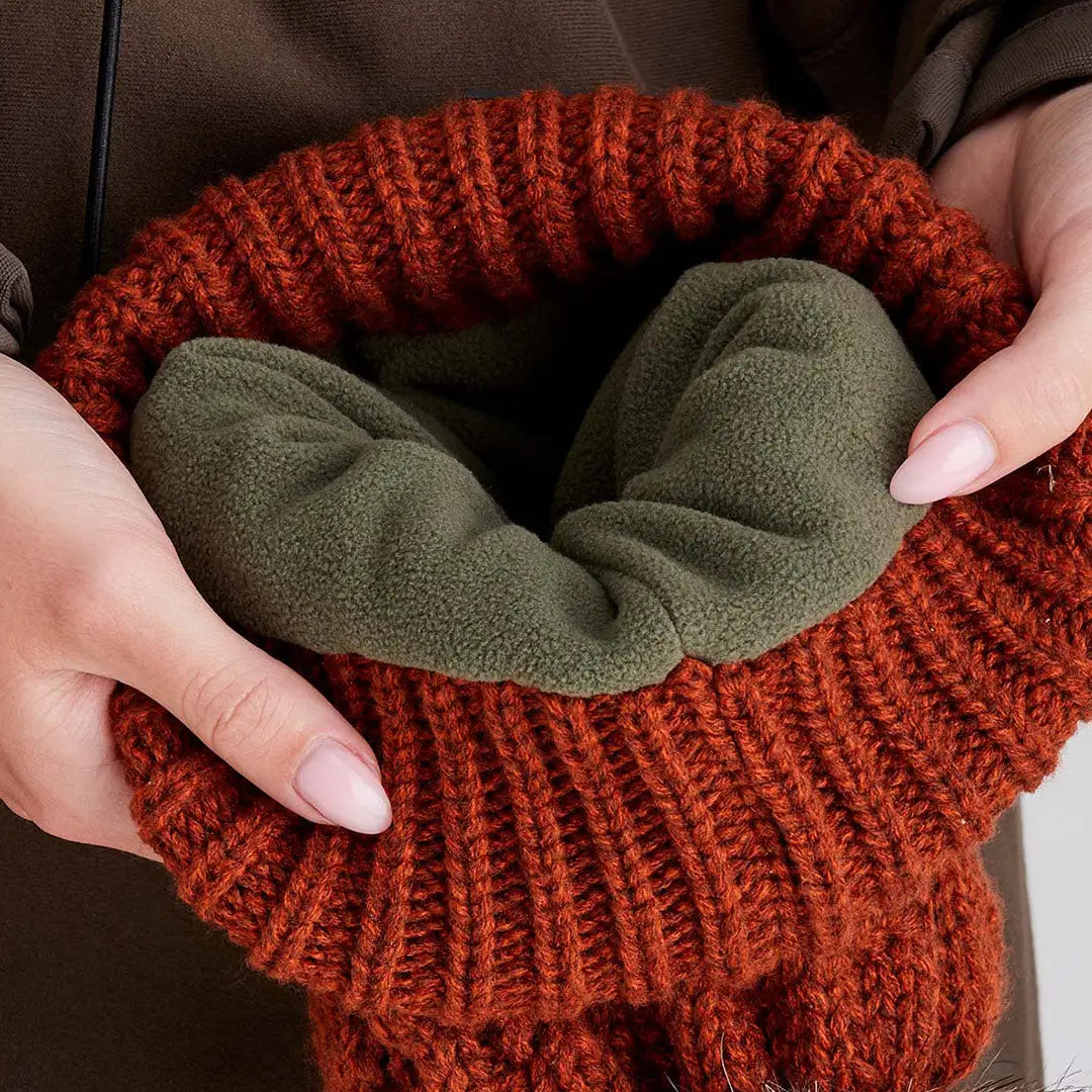 Close-up of a person holding open a rust-orange Ridgeline Nordic Fleck Bobble Hat showing olive-green fleece lining