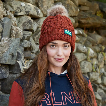 Woman wearing a rust-colored Nordic Fleck Bobble Hat with fur pom-pom