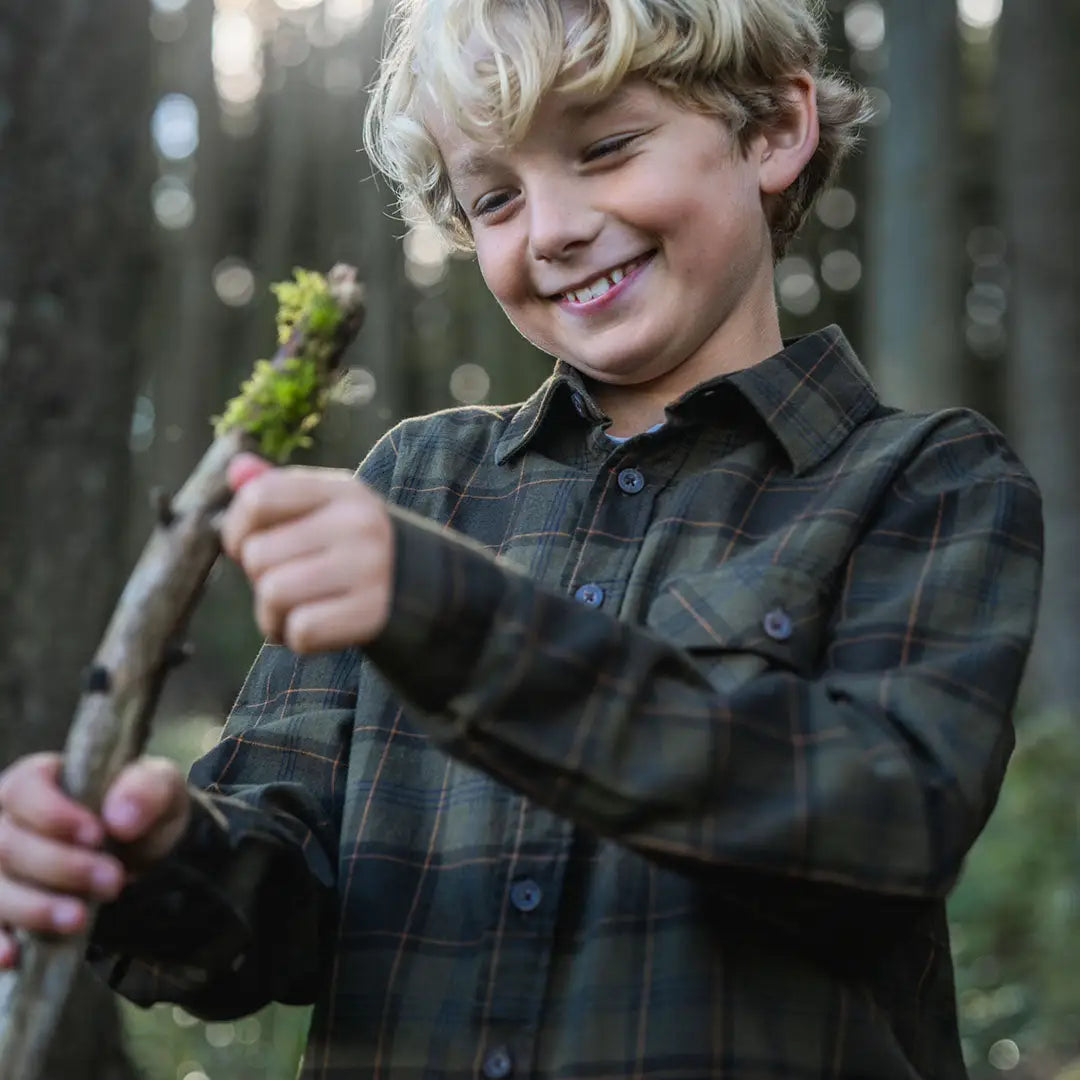 Smiling boy wearing Seeland Glen Junior Flannel Shirt holding mossy stick outdoors