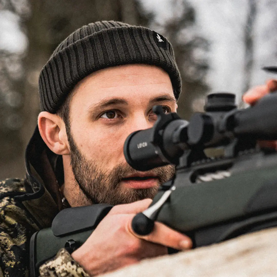 Man aiming rifle with scope wearing Seeland Norite Beanie for outdoor adventures