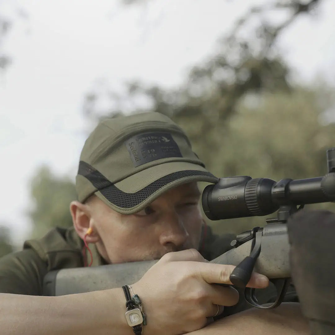 Sniper aiming rifle with scope next to Seeland Selous Cap for hunting country clothing