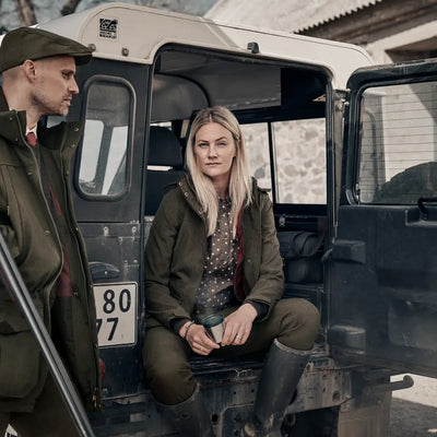 Military vehicle with open doors and two people inside wearing the Woodcock Advanced Jacket