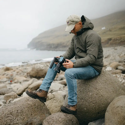 Person on rocky shore wearing a Snugpak Torrent Jacket with binoculars in hand