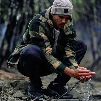 Man in plaid jacket and beanie crouching with water wearing Swanndri Hudson Wool Hoodie