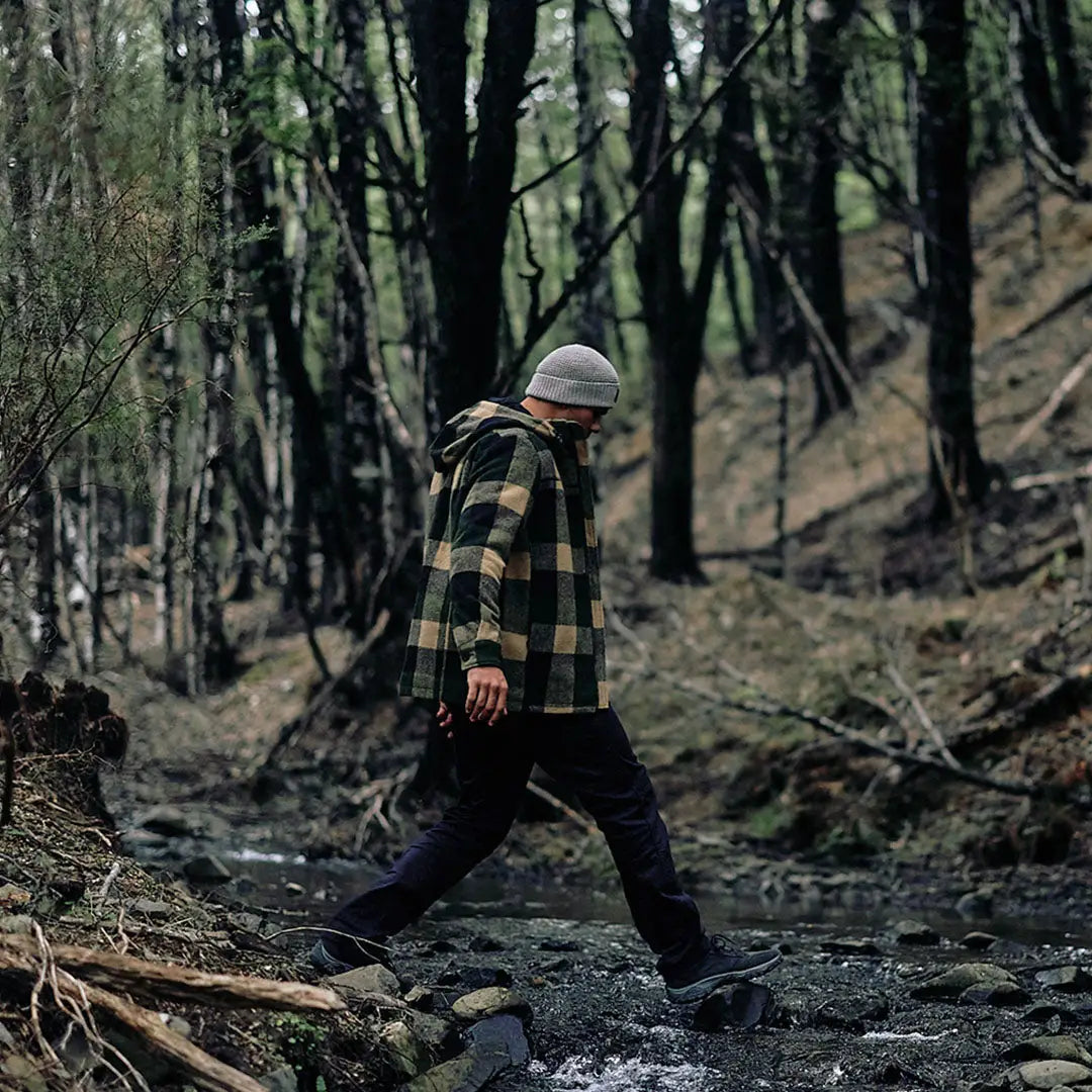 Person crossing rocky stream in Swanndri Hudson Wool Hoodie and beanie outdoor style