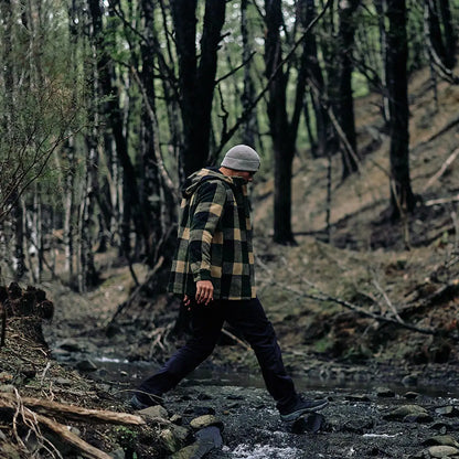 Person crossing rocky stream in Swanndri Hudson Wool Hoodie and beanie outdoor style