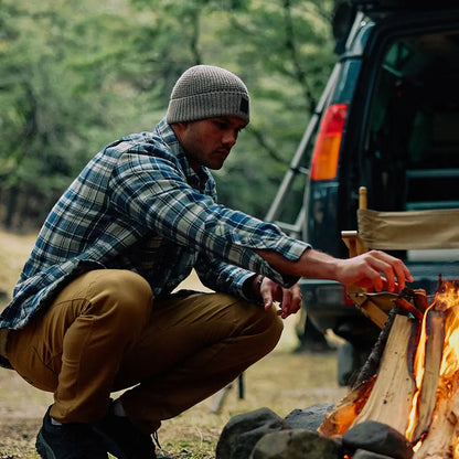 Man in plaid shirt and swanndri newton beanie tending campfire outdoors