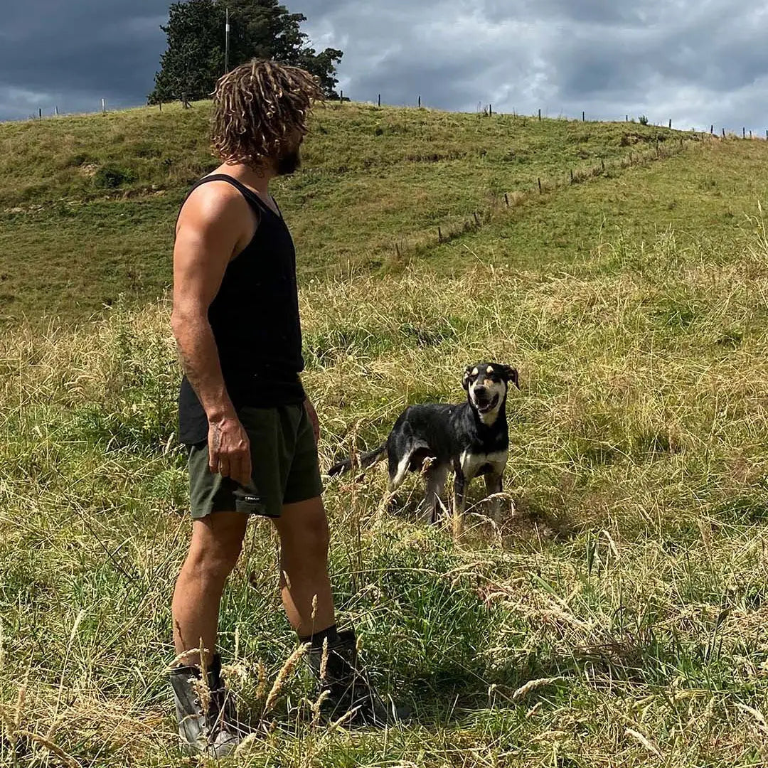 Man and dog in grassy field wearing Swazi Trojan Shorts for a casual outdoor vibe